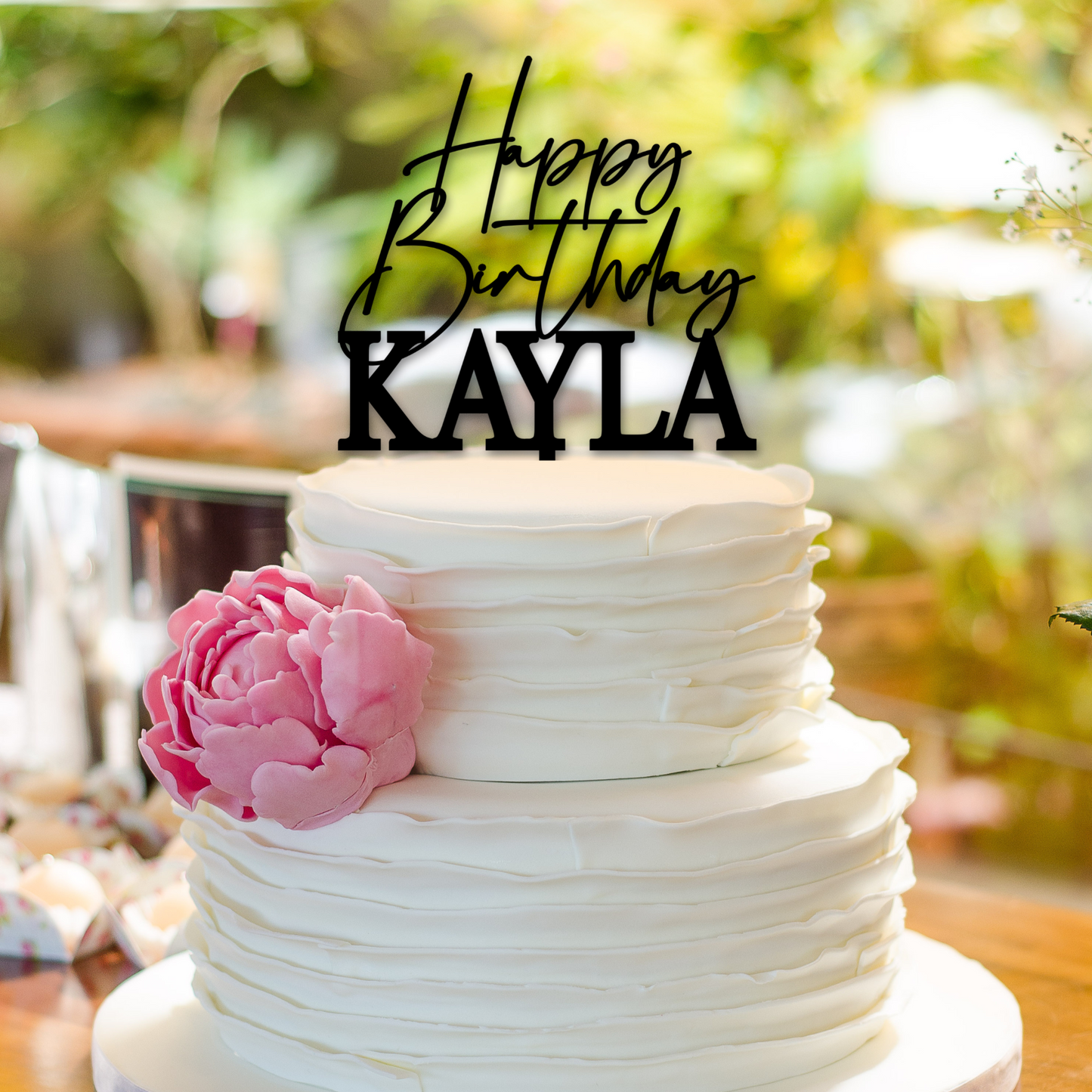 personalized happy birthday cake topper in black on a white tiered cake with pink flower