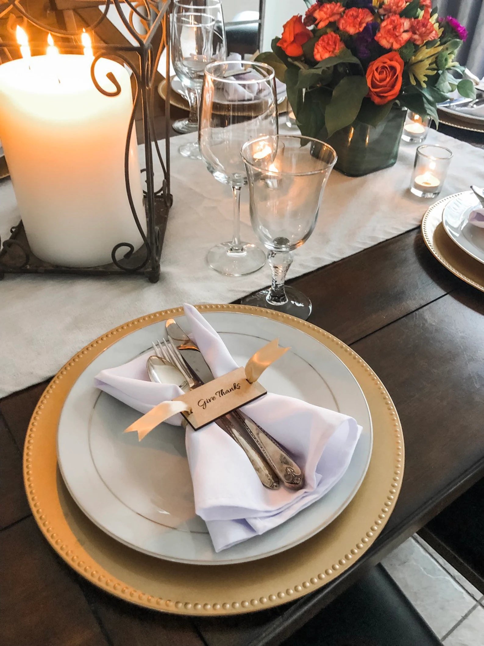 Dining table setting with plates, cutlery, Give Thanks Napkin Holders and a candle on a wooden table.