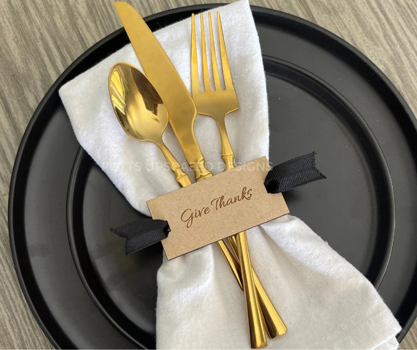 Gold cutlery set on a black plate with a 'Give Thanks' tag.
