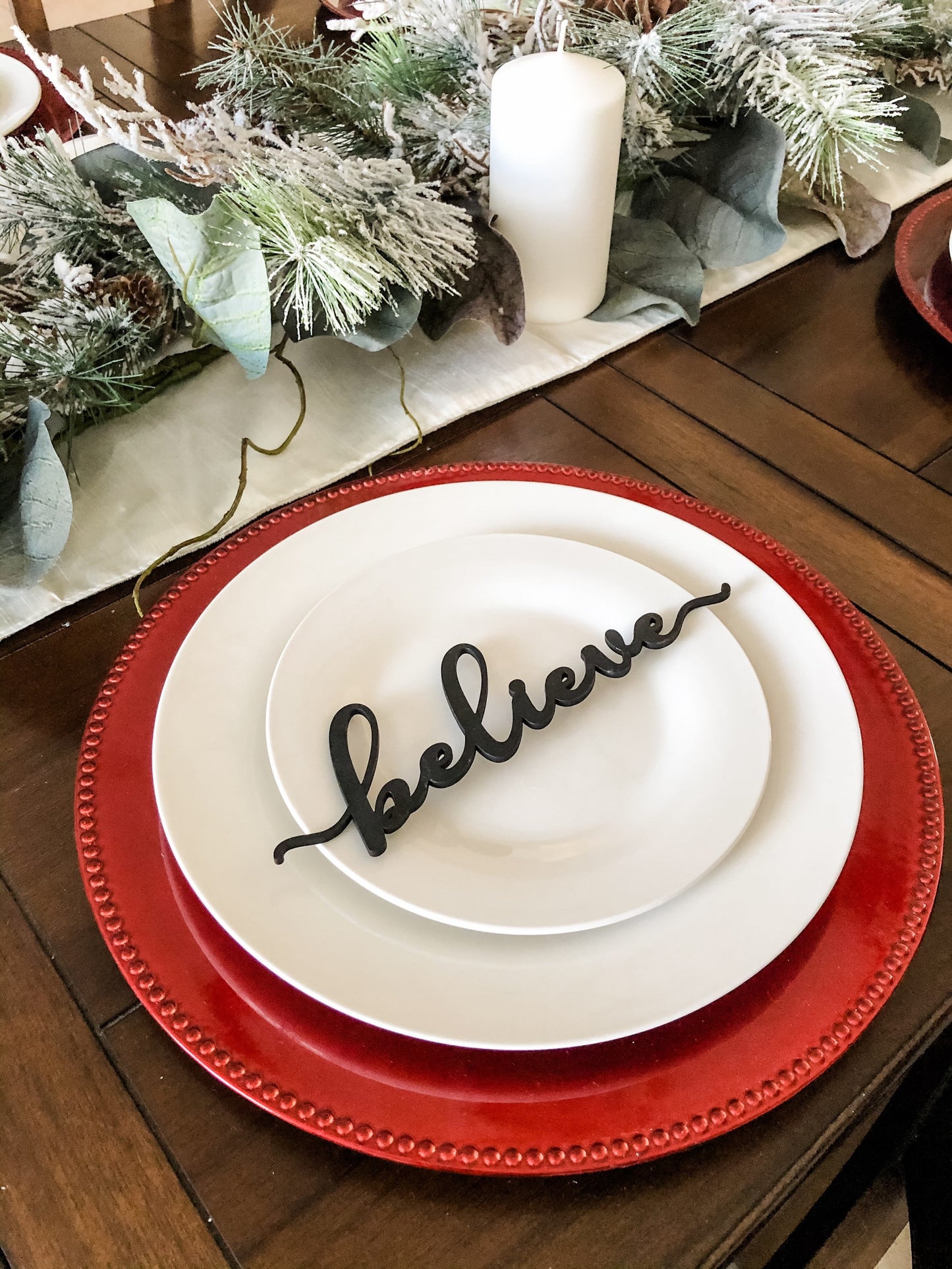 black believe place card on white plates and red charger with snow flocked pine needles and white candles centerpiece to decorate a christmas table