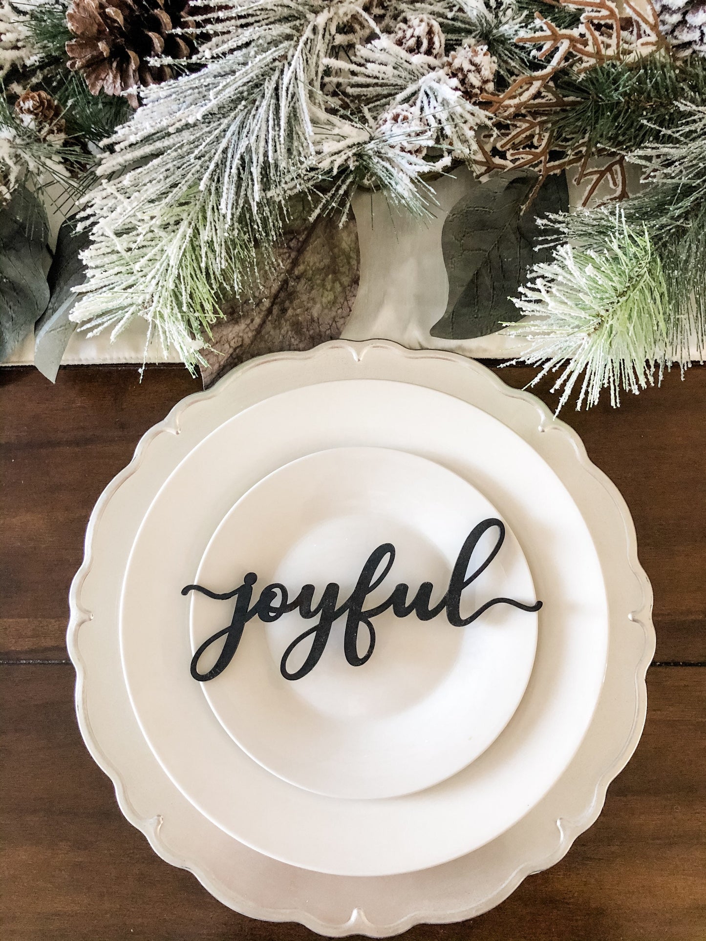 black joyful guest place cards to decorate white plates silver charger and snow flocked pine needles and pine cone centerpiece for christmas table decor