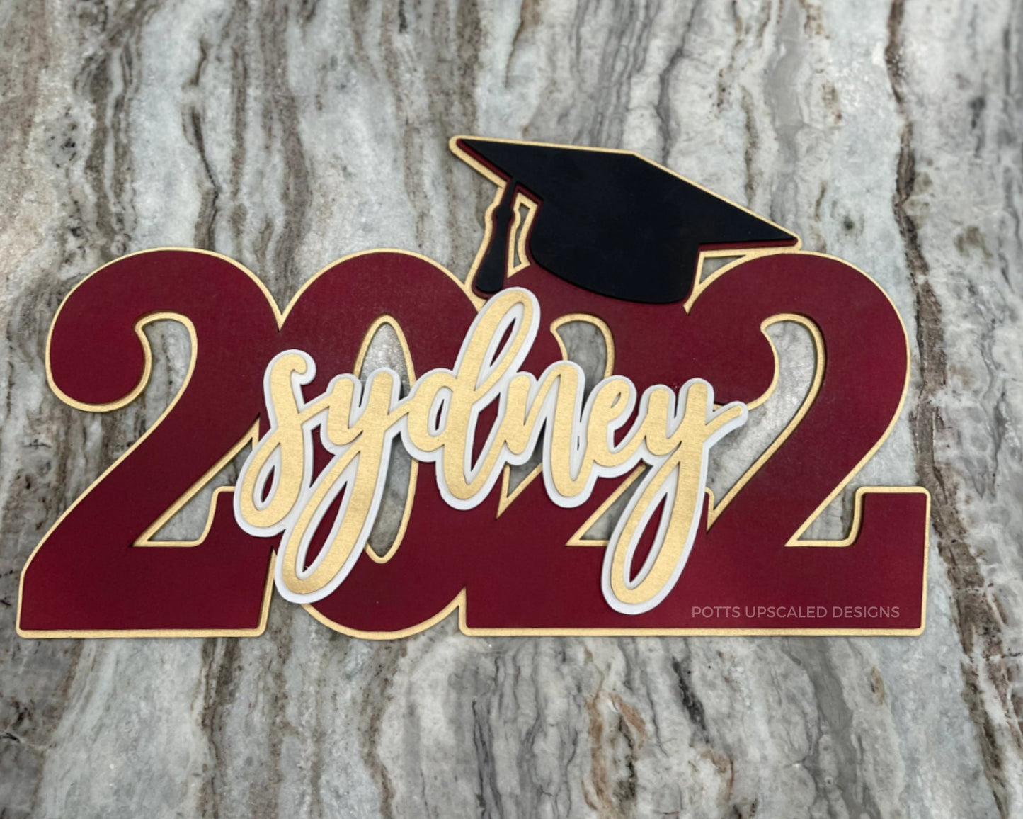 personalized graduation sign 2022 in maroon sydney in gold and a black graduation cap created for senior night gifts and graduation party decor by Potts Upscaled Designs LLC