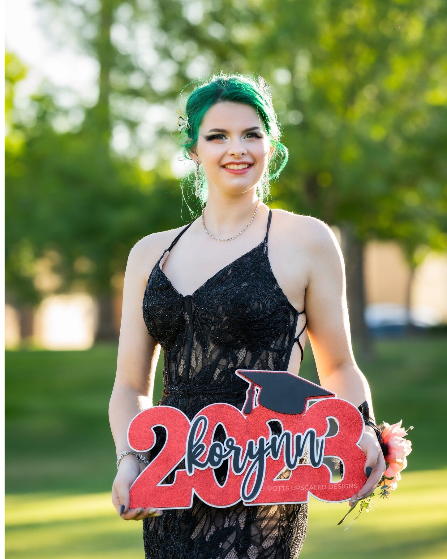 senior graduate in a black lace dress holding a personalized graduation sign prop in red black and silver for senior pictures and graduation party decor