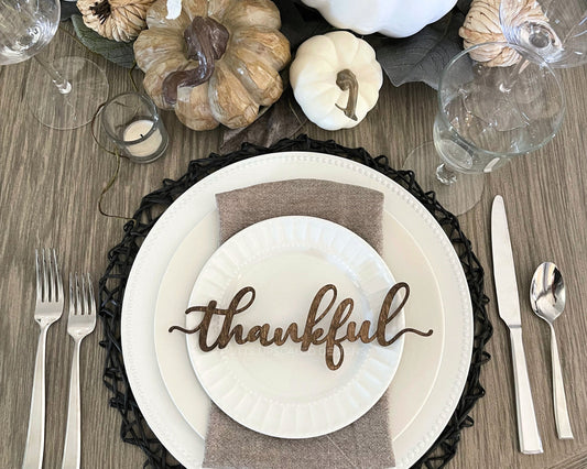 Thankful place card in walnut wood on white plates with pumpkin centerpiece decorating a thanksgiving table