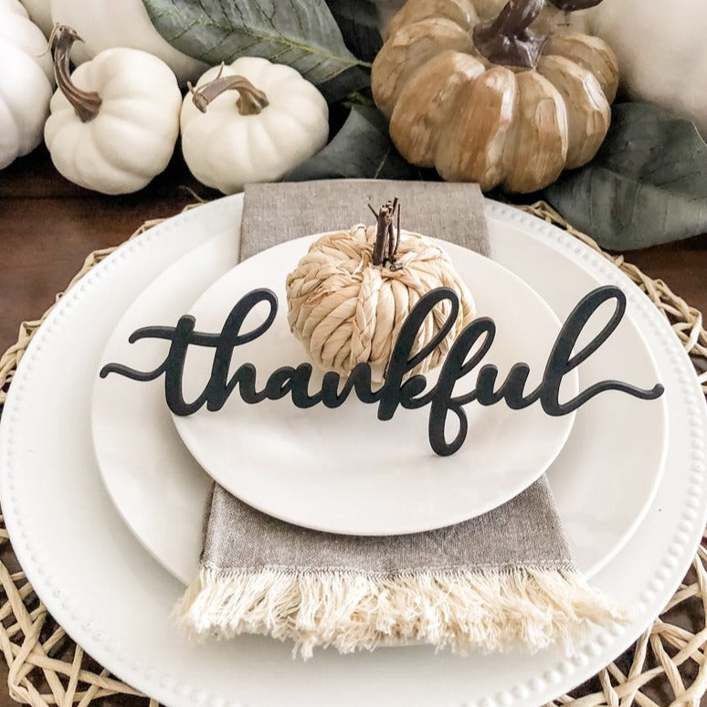 black thankful place card on a thanksgiving table decorated with white plates and white pumpkin centerpiece