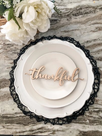 birch wood thankful place card on white plates black woven charger and white flower centerpiece
