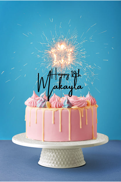 personalized happy birthday cake topper on a pink cake with a blue background.  Star sparkler candle on a white cake plate stand.  happy 18th cake topper in black