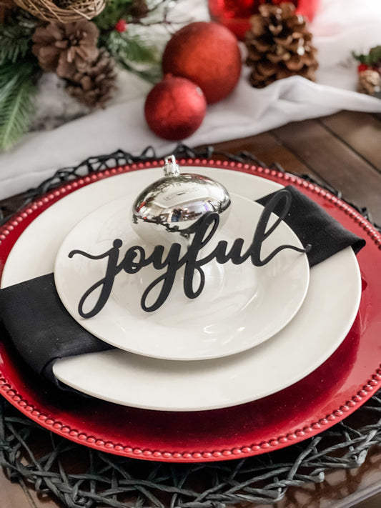 black joyful place card on white plates red charger plate and black napkin with a silver christmas ornament for holiday dinner decor